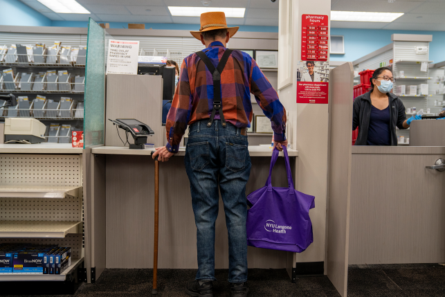 Photo, back of man with cane standing at pharmacy counter
