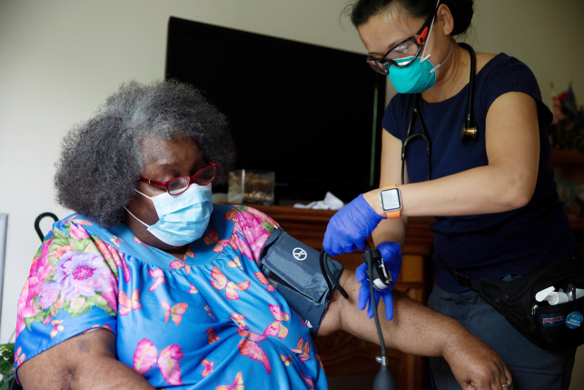 A doctor examines a patient in her home, both in masks