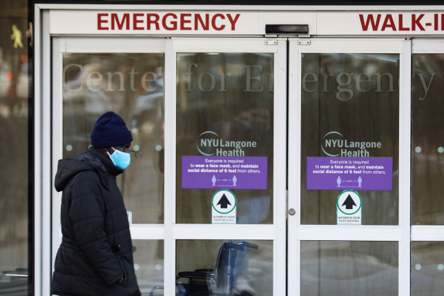 Pedestrian in mask walks by emergency room doors