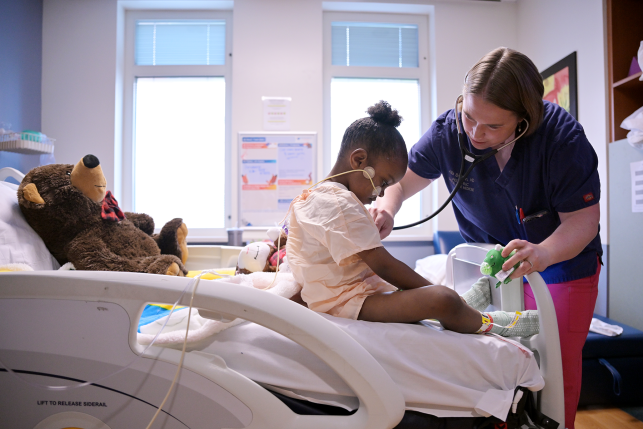 Doctor uses stethoscope on young girl in hospital bed