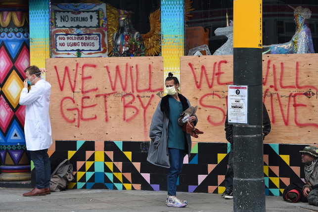 Stuart Malcolm (L), a doctor with the Haight Ashbury Free Clinic, puts on a mask before speaking with homeless people in front of a boarded-up shop.