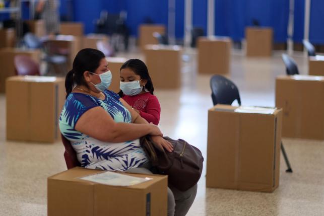 Verenice Gonzalez waits with her daughter in a large room after receiving a COVID-19 vaccine at a clinic in Immokalee, Florida.