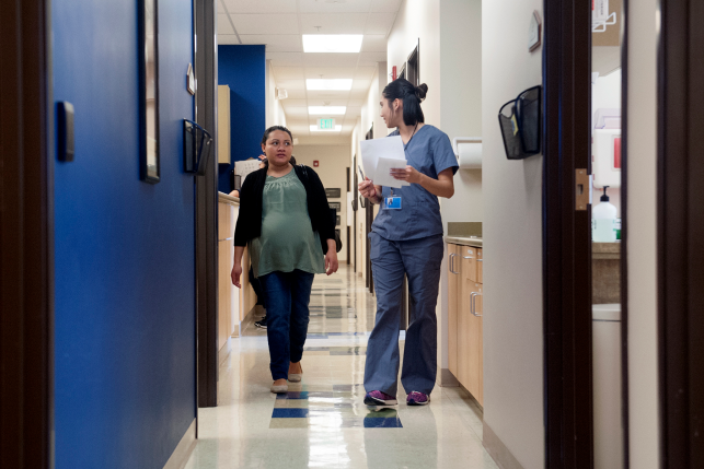 Photo, pregnant woman walks down hallway with hospital staff member