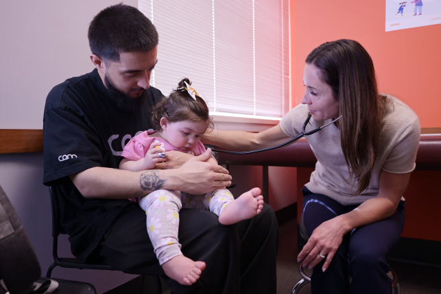 Girl toddler being examined by doctor while sitting on father’s lap