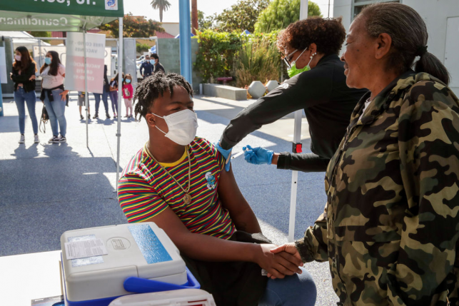Kalvin Green, 15, holds the hand of his mother Marilyn Green as nurse Marie Eddins administers a COVID-19 vaccine at a mobile clinic on June 24, 2021, in Los Angeles