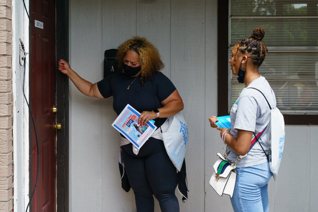 Outreach volunteers knock on a door to inform residents about an upcoming COVID-19 vaccination event