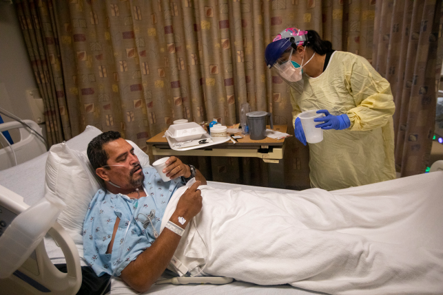 Patient in bed is treated by nurse in mask and full protective gear