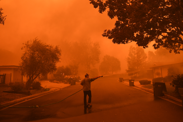 Man sprays with hose a house on fire in smoky neighborhood