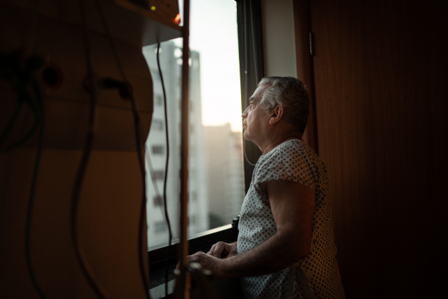 Senior man stares out hospital window at building