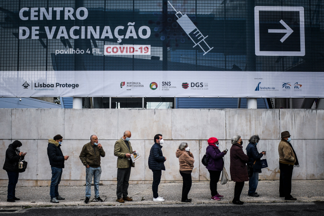 Masked people stand in line for vaccine in front of vaccination sign in Portuguese