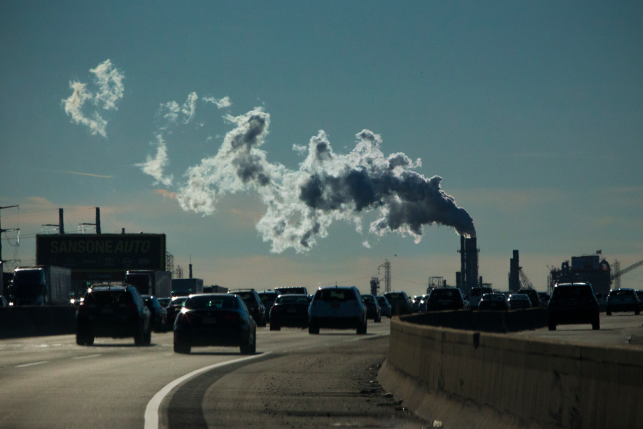 Photo, cars on highway underneath plume of factory smoke