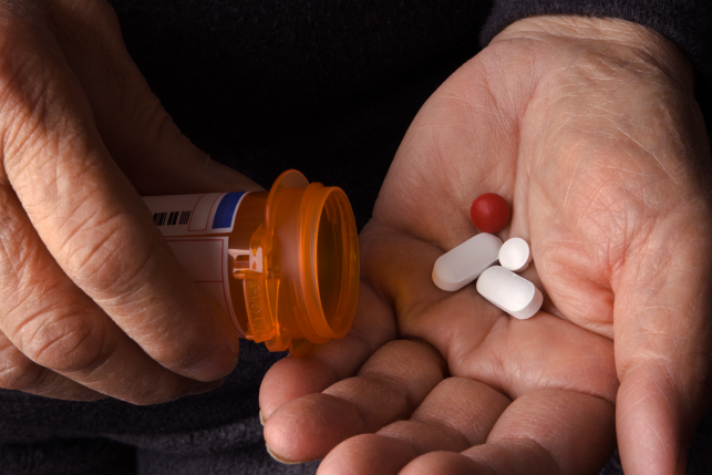 Close-up of senior adult hands holding prescription pill bottle and pouring out drug medications into palm. 