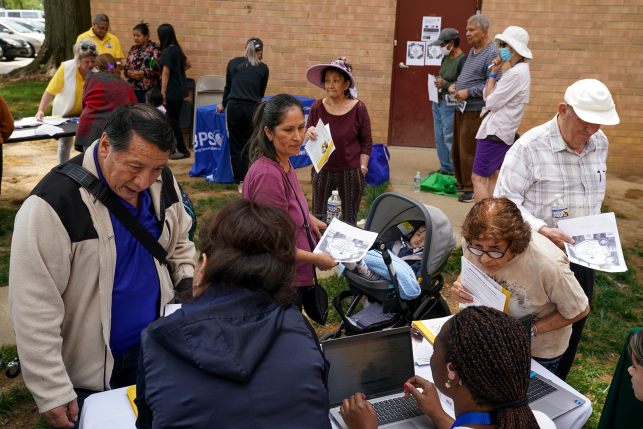 Photo, group of people get paperwork from workers at laptops