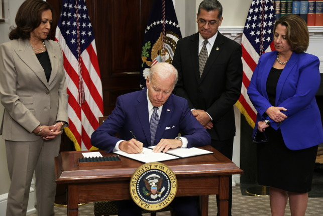 President Biden signing paperwork in front of American flags