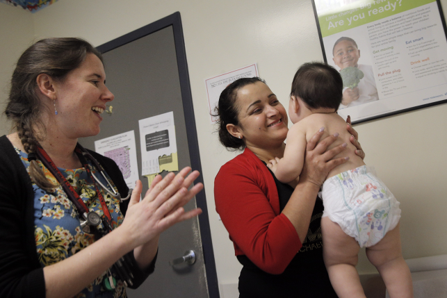 Photo, woman holds baby while nurse claps with smile