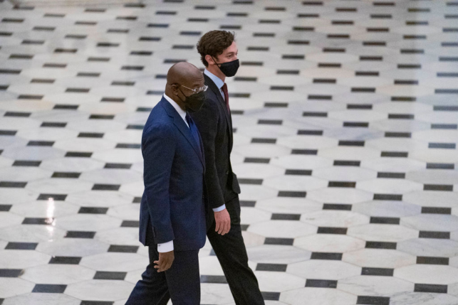 Senators Warnock and Ossoff walk across a black and white floor