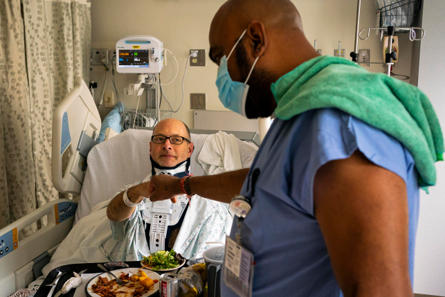 Hospital worker fist-bumps patient in hospital bed