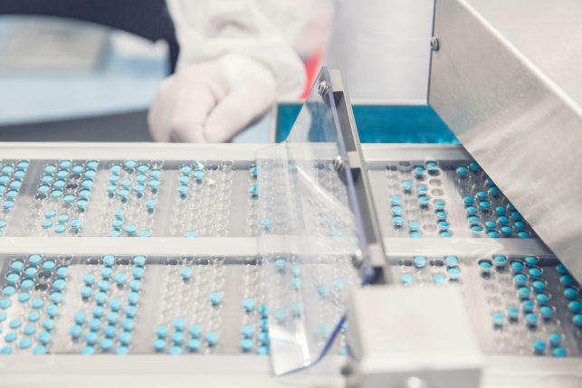 blue pills in machine manufactured with white gloved hand in background