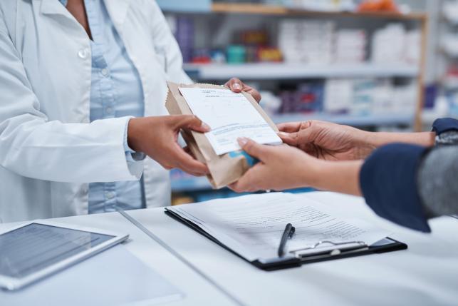 Pharmacist handing a customer a prescription package.