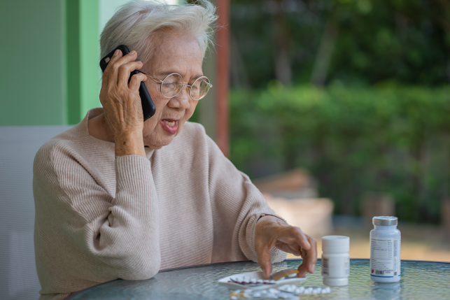 senior woman on phone looks at pill packets on table