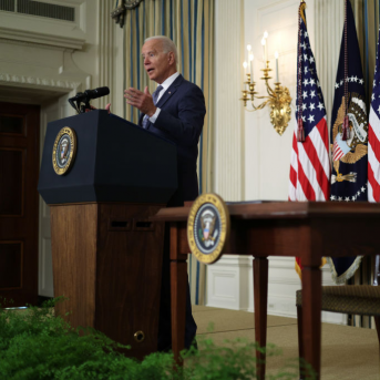 President Biden speaking at podium in front of American flags and white house seal.