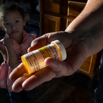 Hand holds out prescription bottle in front of young girl