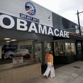 Woman walks in front of storefront that reads Obamacare