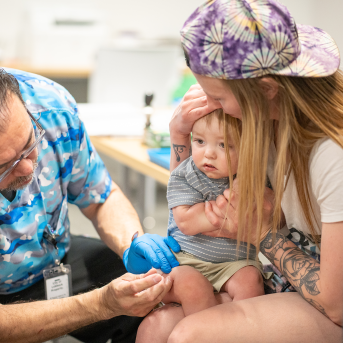 Mom holds baby who is receiving vaccination injection.