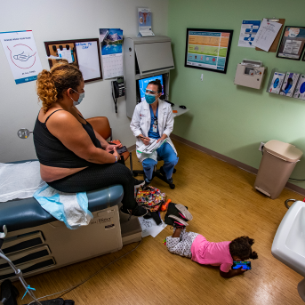Doctor counsels patient on abortion in room with young child on floor playing