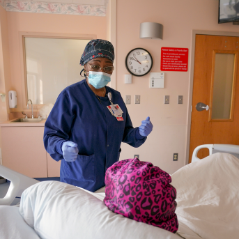 Photo, nurse in mask talks to patient in bed