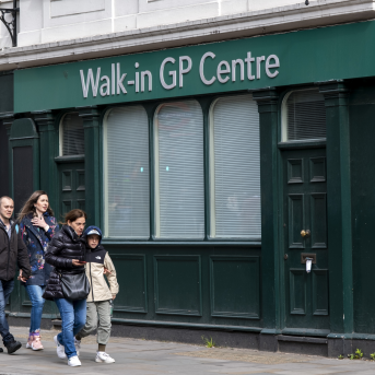 People walking in front of a green building with a sign that reads "Walk-in GP Centre"