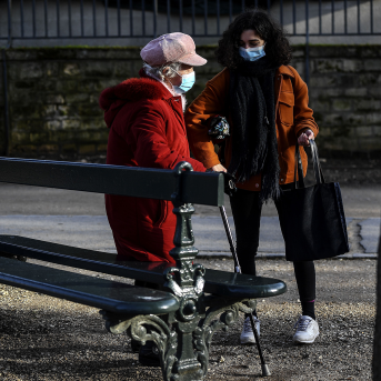 Elderly woman in mask is helped by young woman in park