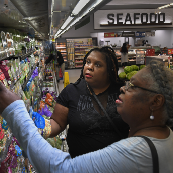 Two women in grocery store look at bagged lettuce