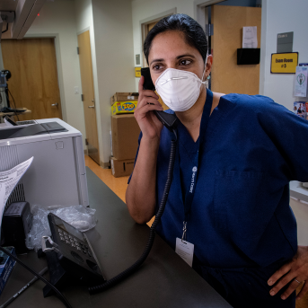 Female physician in scrubs and mask on phone in hospital