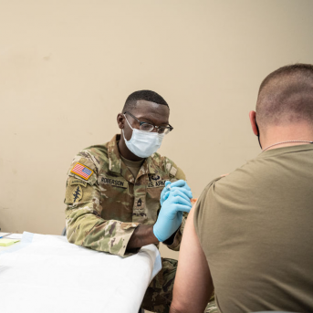 Military doctor gives vaccine to other military member at white table