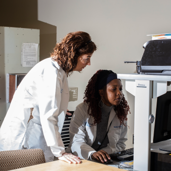 Two lab coat-wearing employees work on computer
