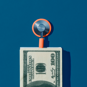 Photograph of stethoscope coming out of a pile of hundred US dollar bills