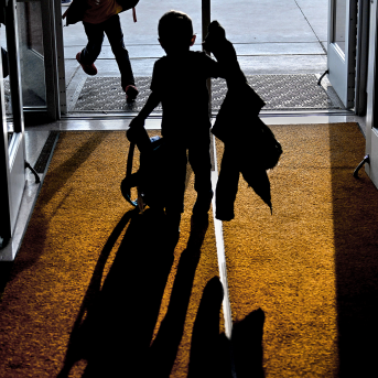 Photo, silhouette of kid with jacket and backpack in school door