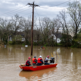 Group of search and rescue workers in a boat surrounded by flood waters in a rural area