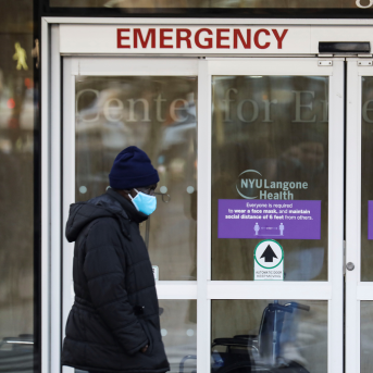 Pedestrian in mask walks by emergency room doors