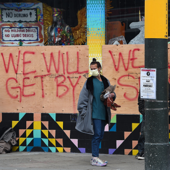 Stuart Malcolm (L), a doctor with the Haight Ashbury Free Clinic, puts on a mask before speaking with homeless people in front of a boarded-up shop.