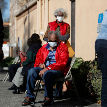 senior man sits in chair waiting in line for vaccine
