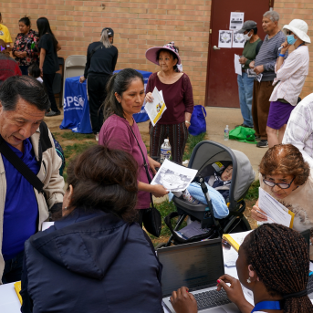 Photo, group of people get paperwork from workers at laptops
