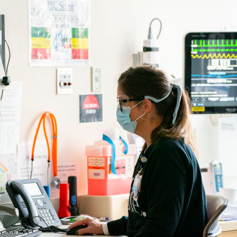 Nurse sits at computer with mask on