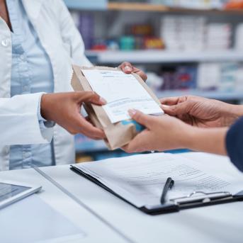 Pharmacist handing a customer a prescription package.