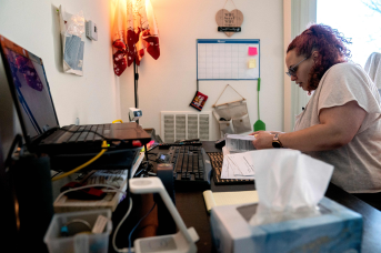 Photo, woman types at computer with paperwork