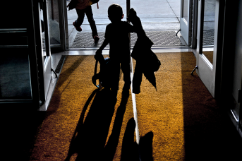 Photo, silhouette of kid with jacket and backpack in school door