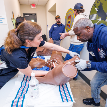 Woman coaching a man through emergency childbirth scenarios with the use of a birthing simulator.