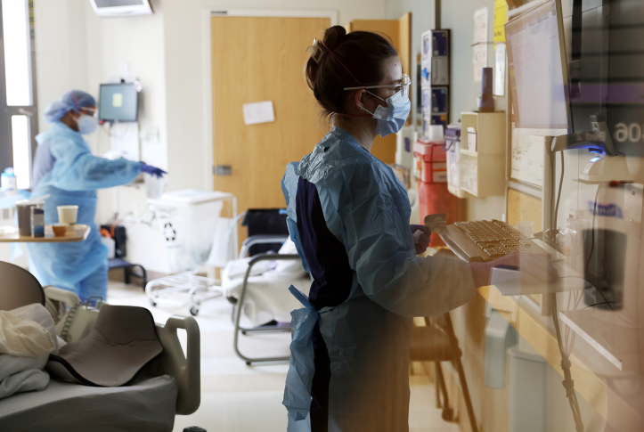 Nurse in full PPE works on computer in ICU.