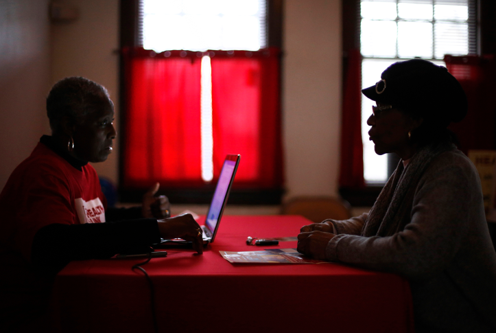 Two people sit on opposite sides of the table while one looks at a laptop